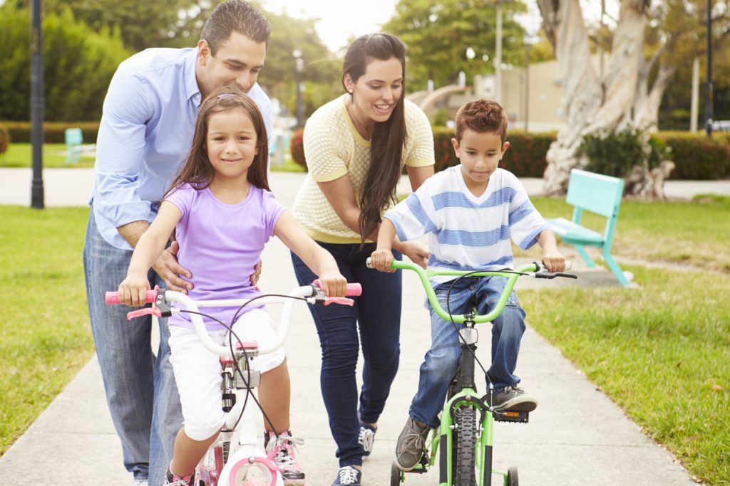 parents teaching children to ride bikes in park
